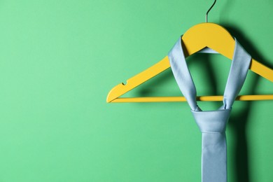 Photo of Hanger with light blue tie on green background, closeup. Space for text