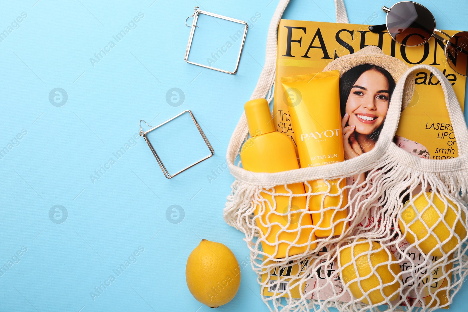 Photo of String bag with magazine, lemons and summer accessories on light blue background, flat lay. Space for text