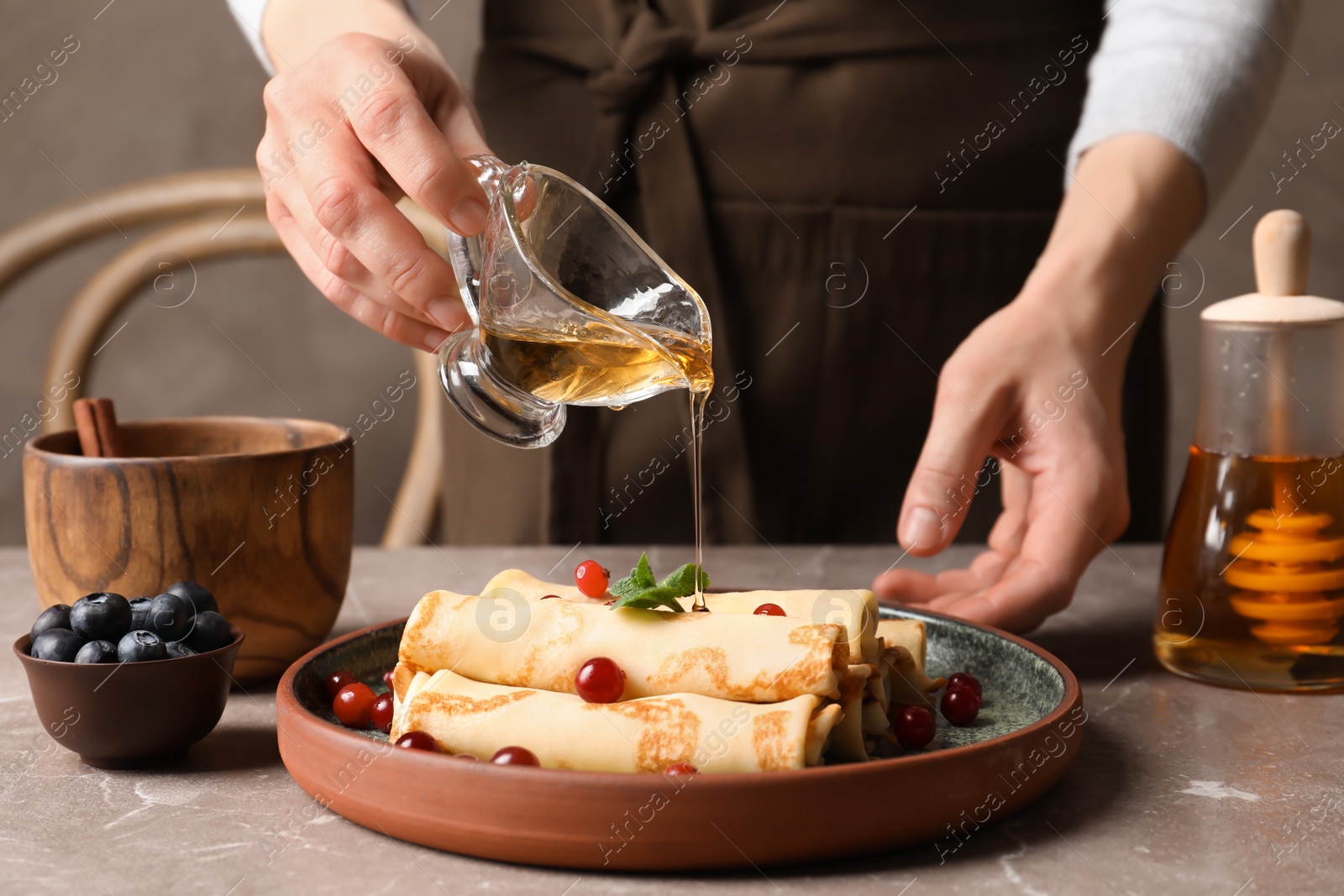 Photo of Woman pouring honey onto thin pancakes with berries at table