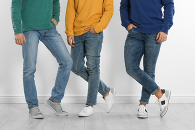 Photo of Group of young men in stylish jeans near white wall, closeup