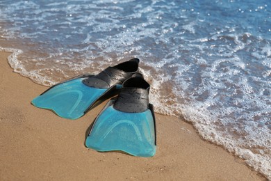 Photo of Pair of turquoise flippers on sand near sea. Space for text