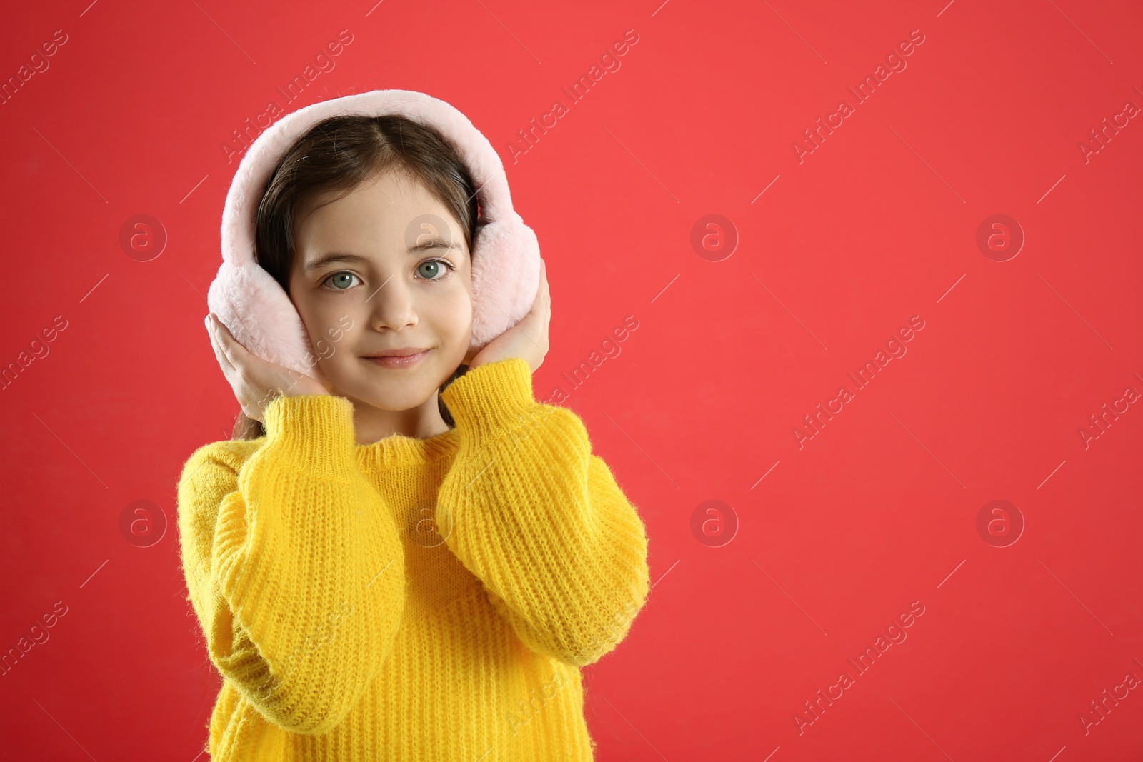 Photo of Cute girl wearing stylish earmuffs on red background. Space for text