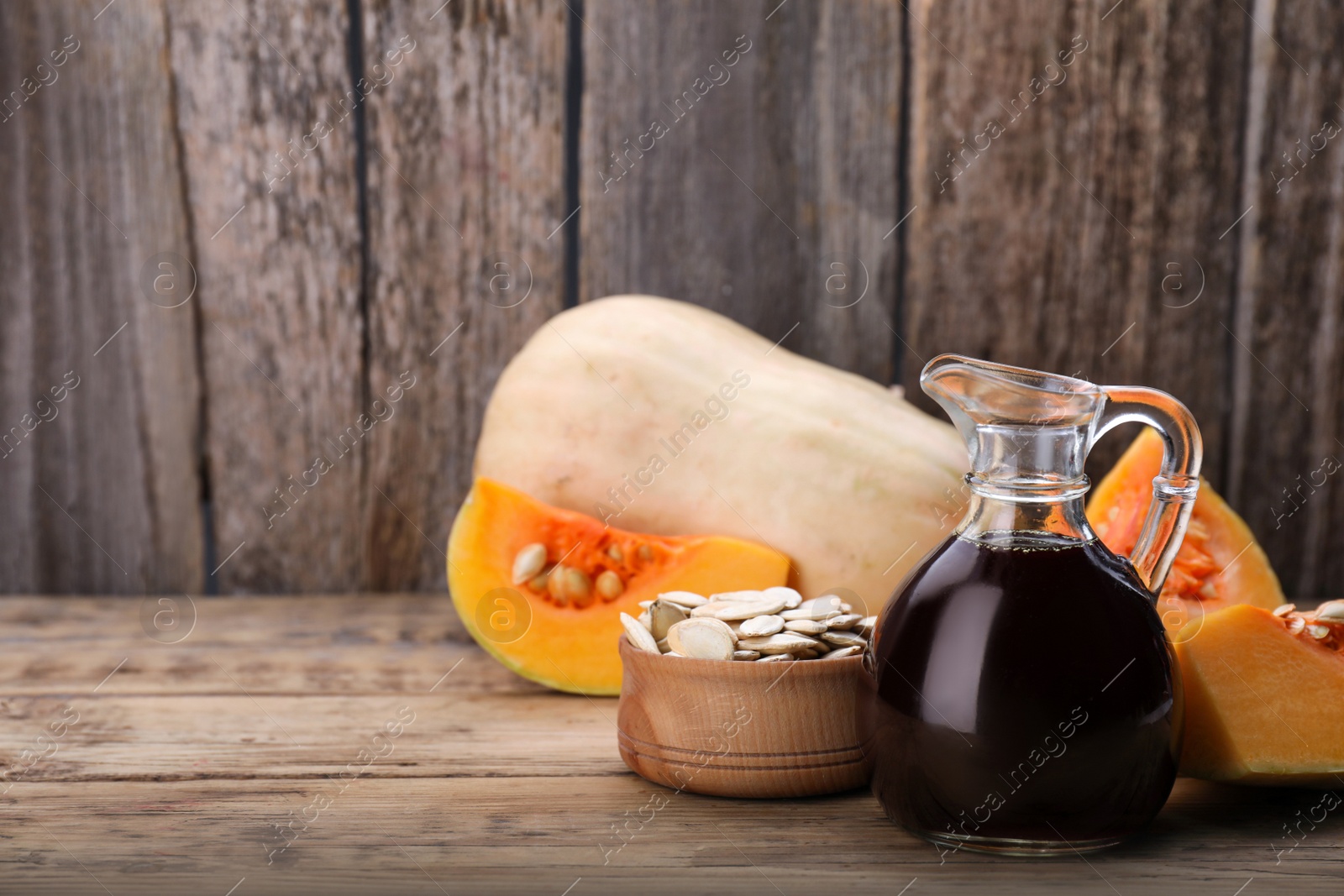 Photo of Fresh pumpkin seed oil in glass jug on wooden table. Space for text