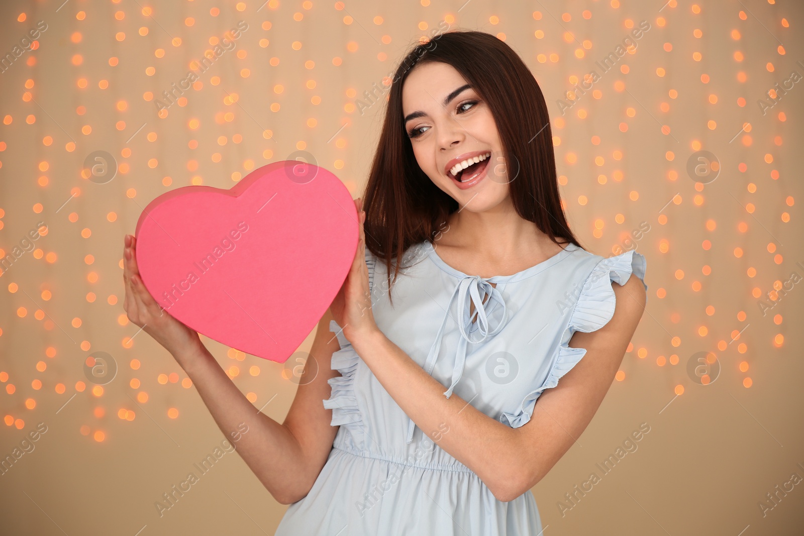 Photo of Portrait of beautiful smiling girl with heart shaped gift box on blurred background. International Women's Day