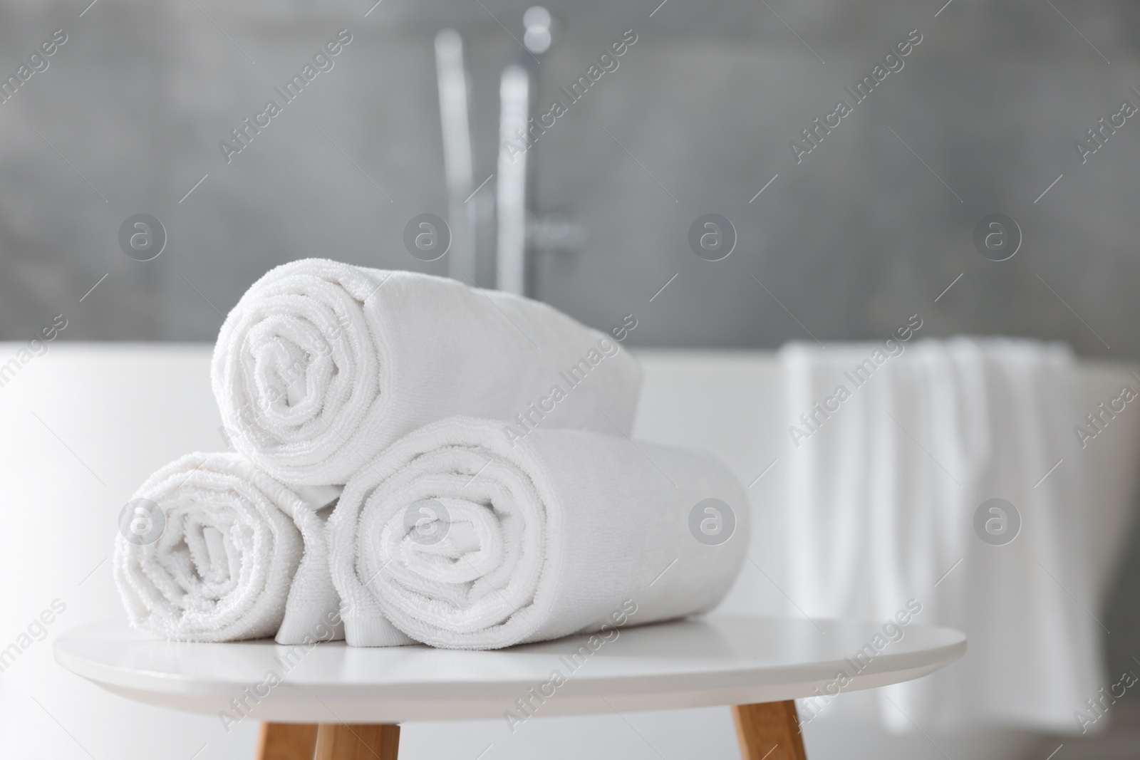 Photo of Rolled white towels on stool in bathroom. Space for text