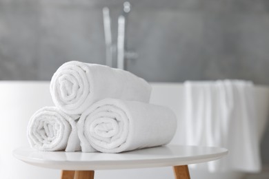 Photo of Rolled white towels on stool in bathroom. Space for text