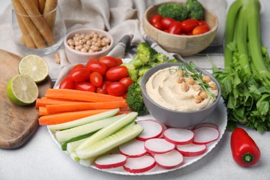 Plate with delicious hummus and fresh vegetables on light grey table, closeup