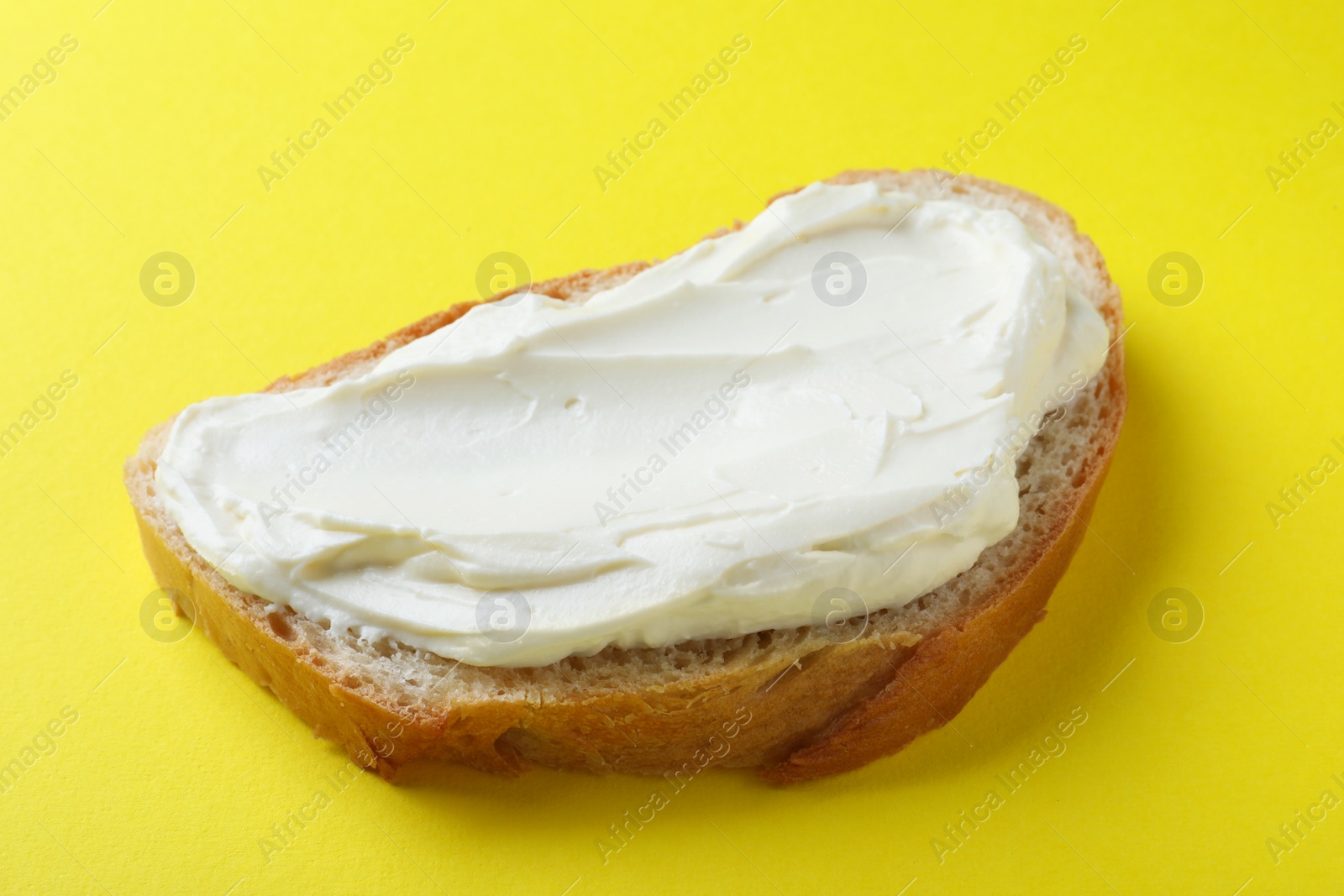 Photo of Slice of bread with tasty cream cheese on yellow background, closeup