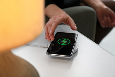 Photo of Woman taking smartphone from wireless charger in room, closeup