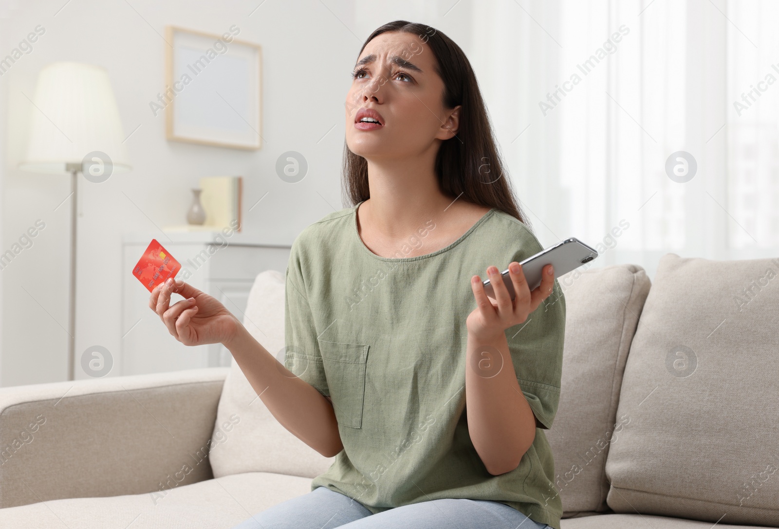 Photo of Confused woman with credit card and smartphone at home. Be careful - fraud