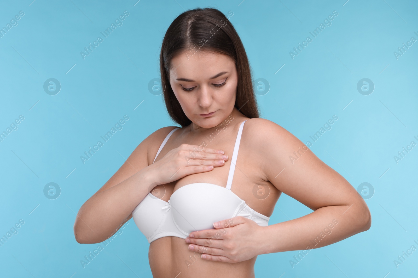 Photo of Mammology. Woman in bra doing breast self-examination on light blue background