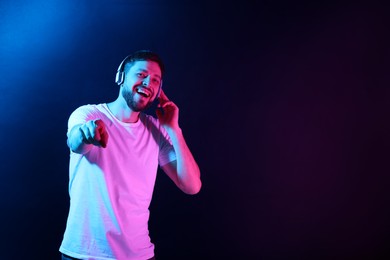 Photo of Happy man in headphones enjoying music in neon lights against dark blue background. Space for text