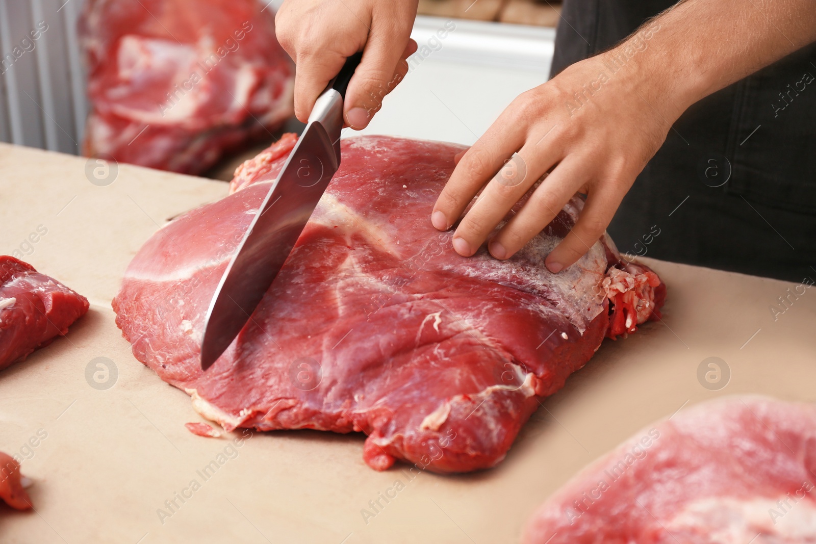 Photo of Butcher cutting fresh raw meat on counter in shop, closeup