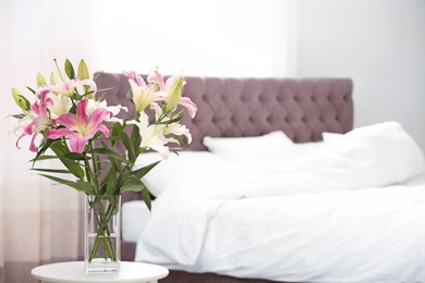 Vase with bouquet of beautiful lilies on table in bedroom. Space for text