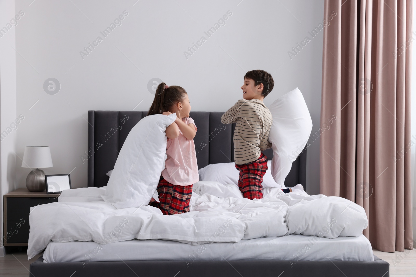 Photo of Brother and sister having pillow fight while changing bed linens in bedroom