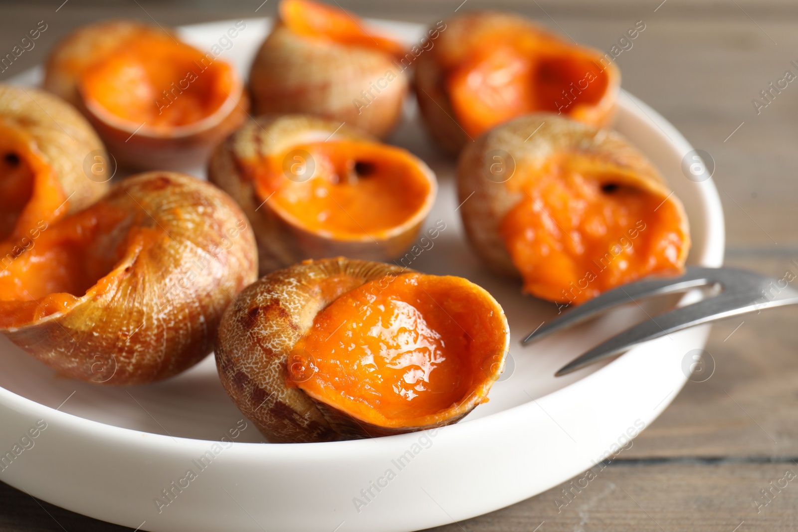 Photo of Delicious cooked snails with fork on table, closeup