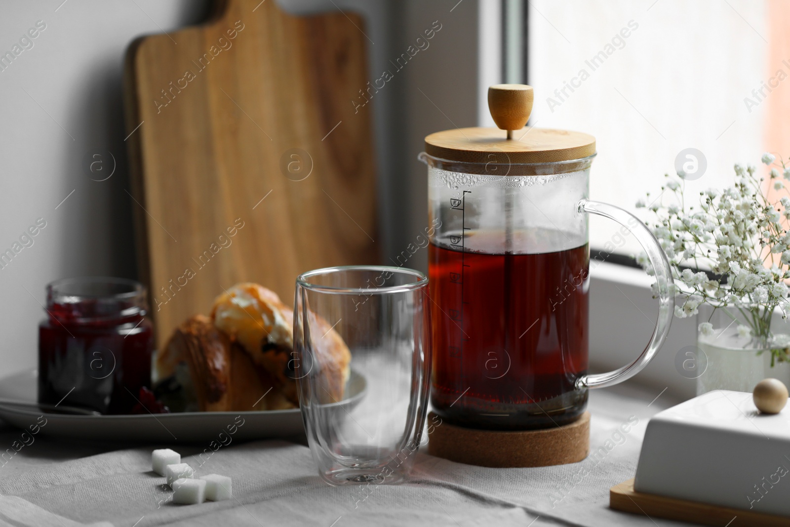 Photo of Teapot with freshly brewed tea, empty glass and sugar cubes on table near window