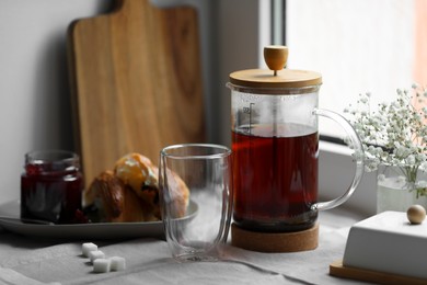 Photo of Teapot with freshly brewed tea, empty glass and sugar cubes on table near window