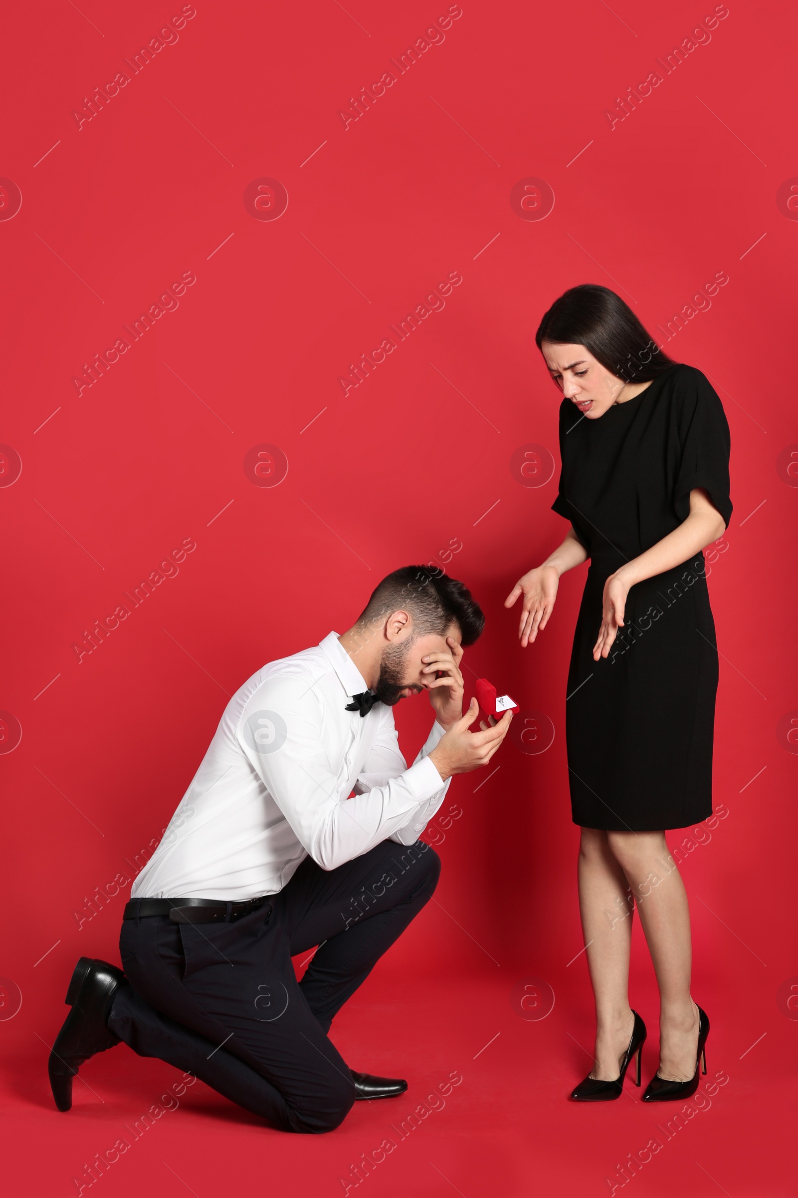 Photo of Young woman rejecting engagement ring from boyfriend on red background