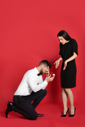 Young woman rejecting engagement ring from boyfriend on red background