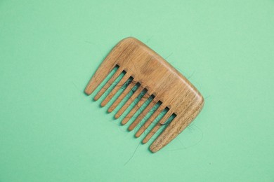 Wooden comb with lost hair on green background, top view