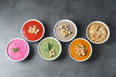 Different tasty cream soups in bowls on dark grey table, flat lay