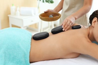 Photo of Beautiful young woman getting hot stone massage in spa salon