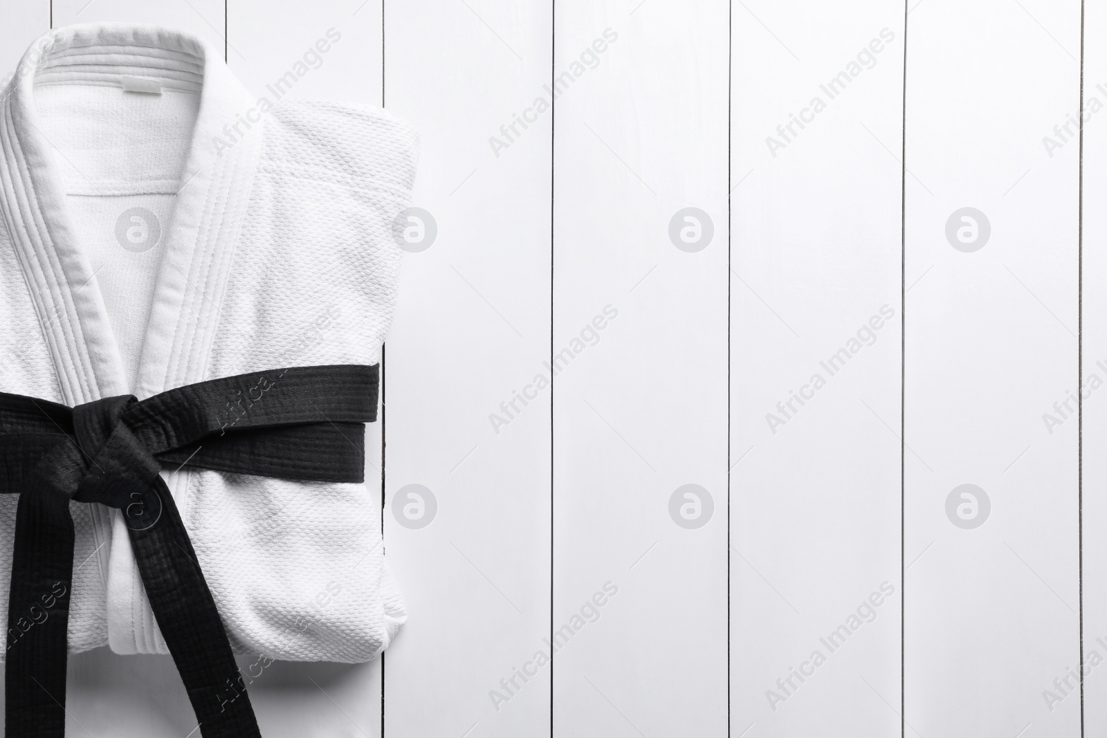 Photo of Martial arts uniform with black belt on white wooden background, top view. Space for text