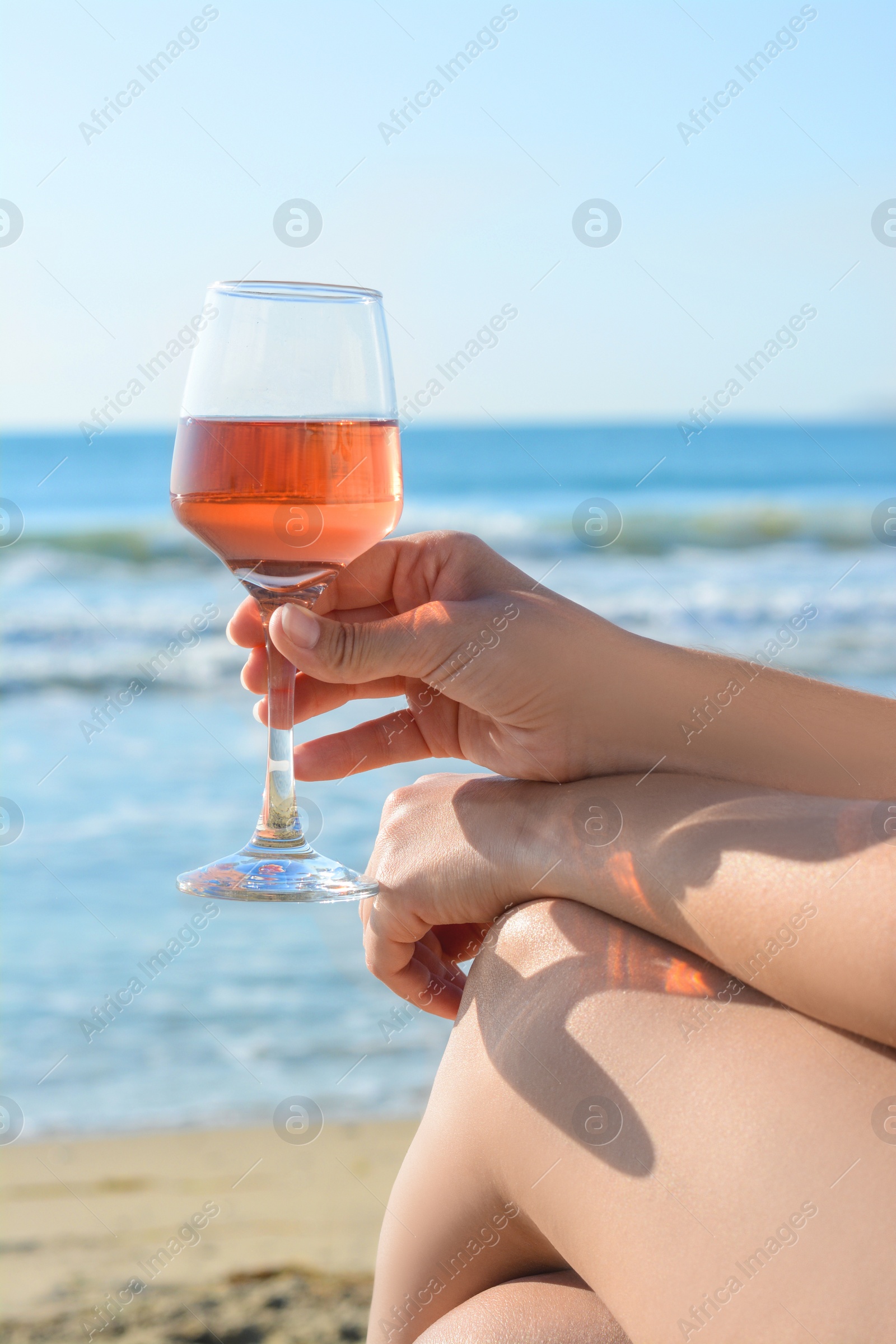 Photo of Woman with glass of tasty rose wine near sea, closeup