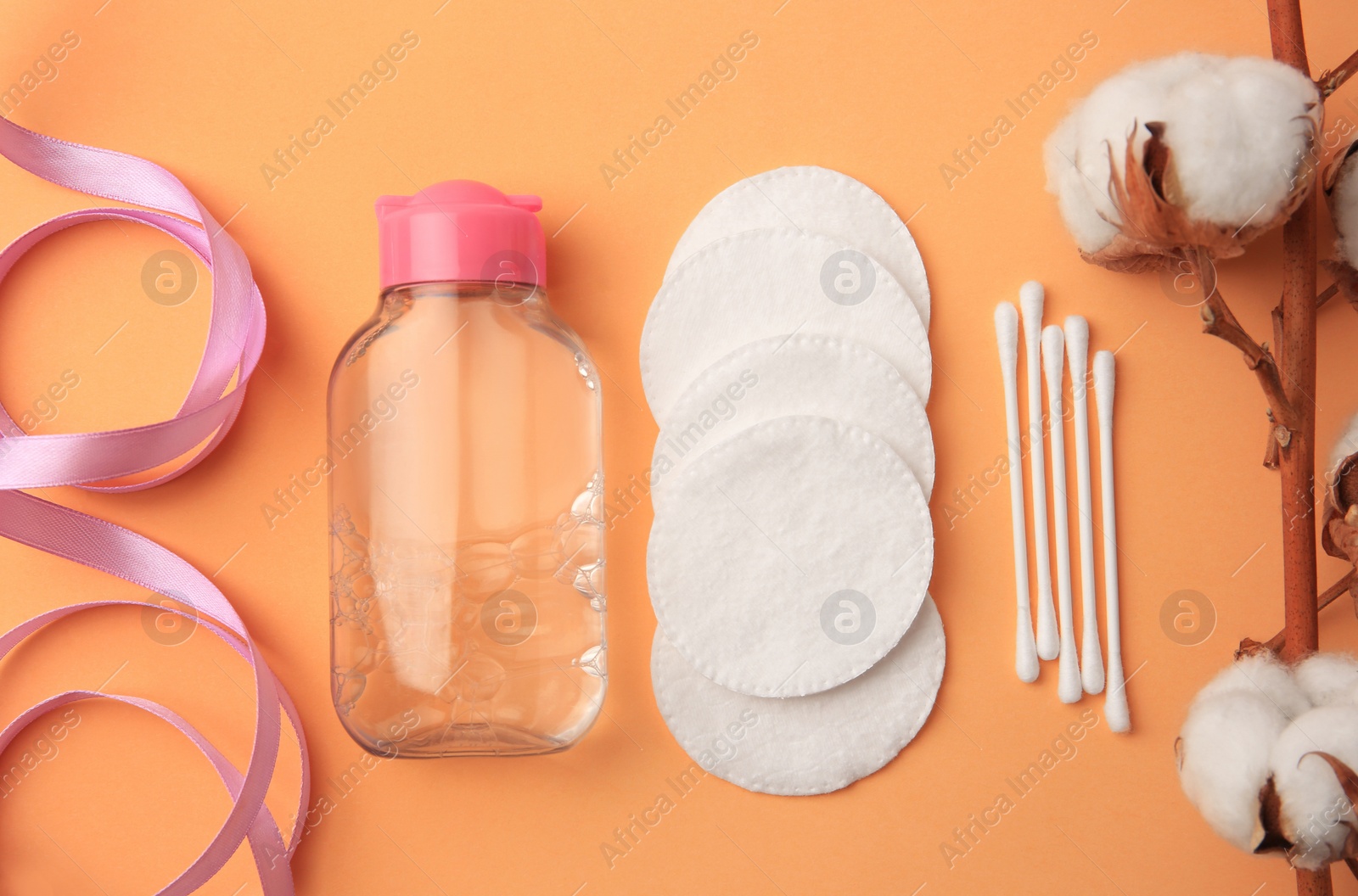 Photo of Flat lay composition with makeup remover and cotton flowers on pale orange background