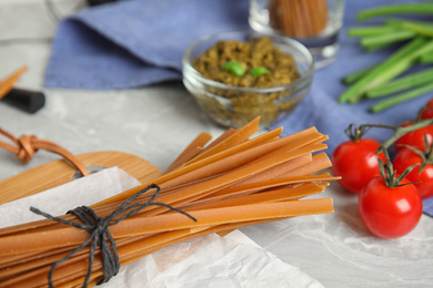 Tied uncooked buckwheat noodles on light grey table, closeup