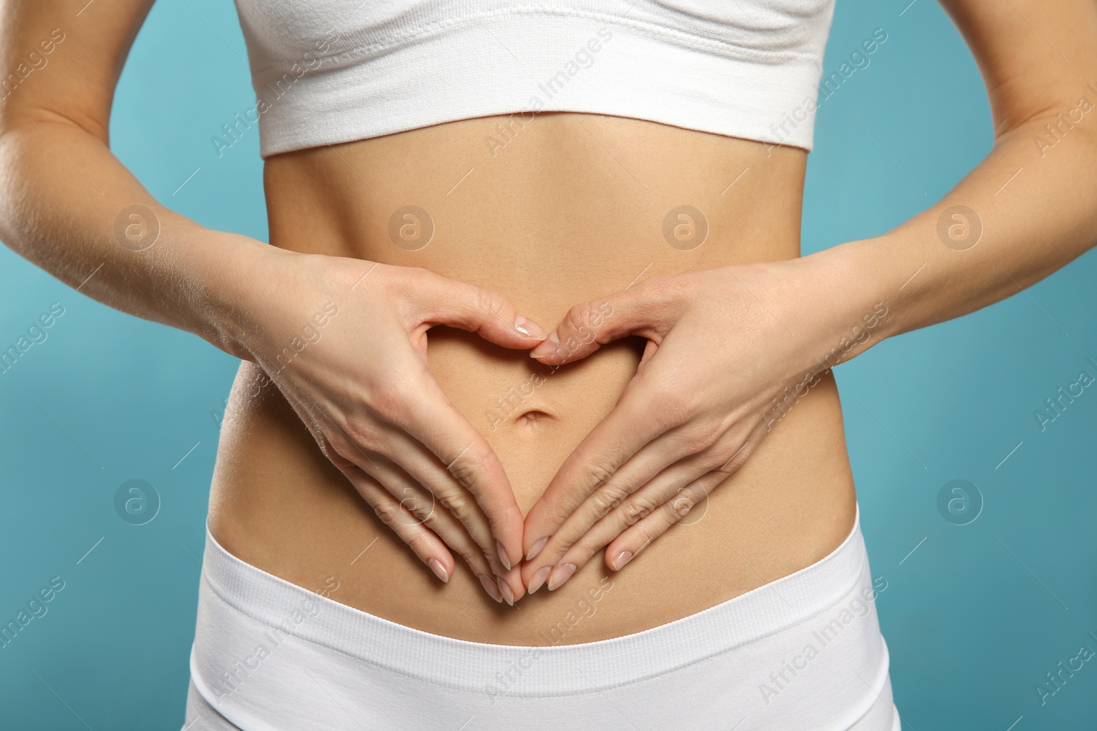 Photo of Woman making heart with her hands on belly against light blue background, closeup