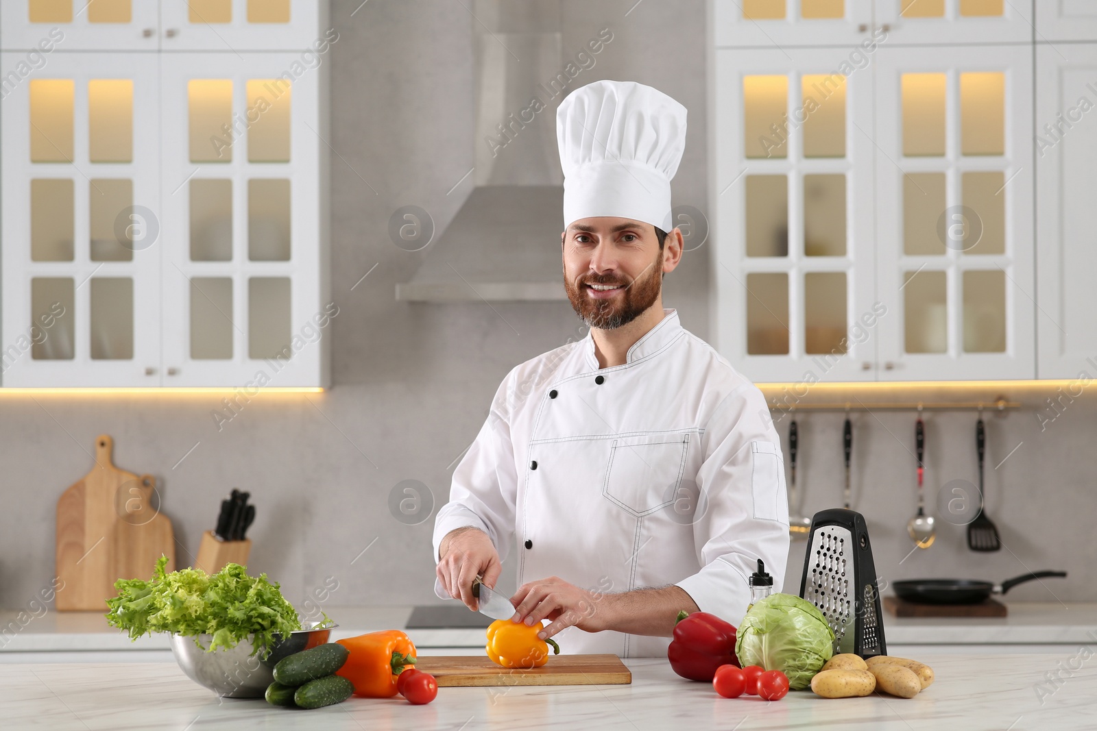 Photo of Chef cutting bell pepper at marble table in kitchen