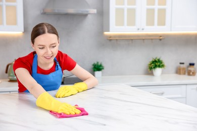 Photo of Woman cleaning white marble table with rag in kitchen, space for text