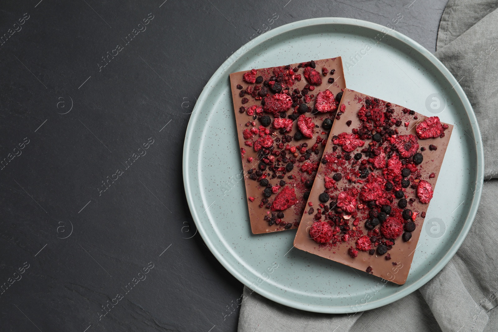 Photo of Chocolate bars with freeze dried fruits on black table, top view. Space for text