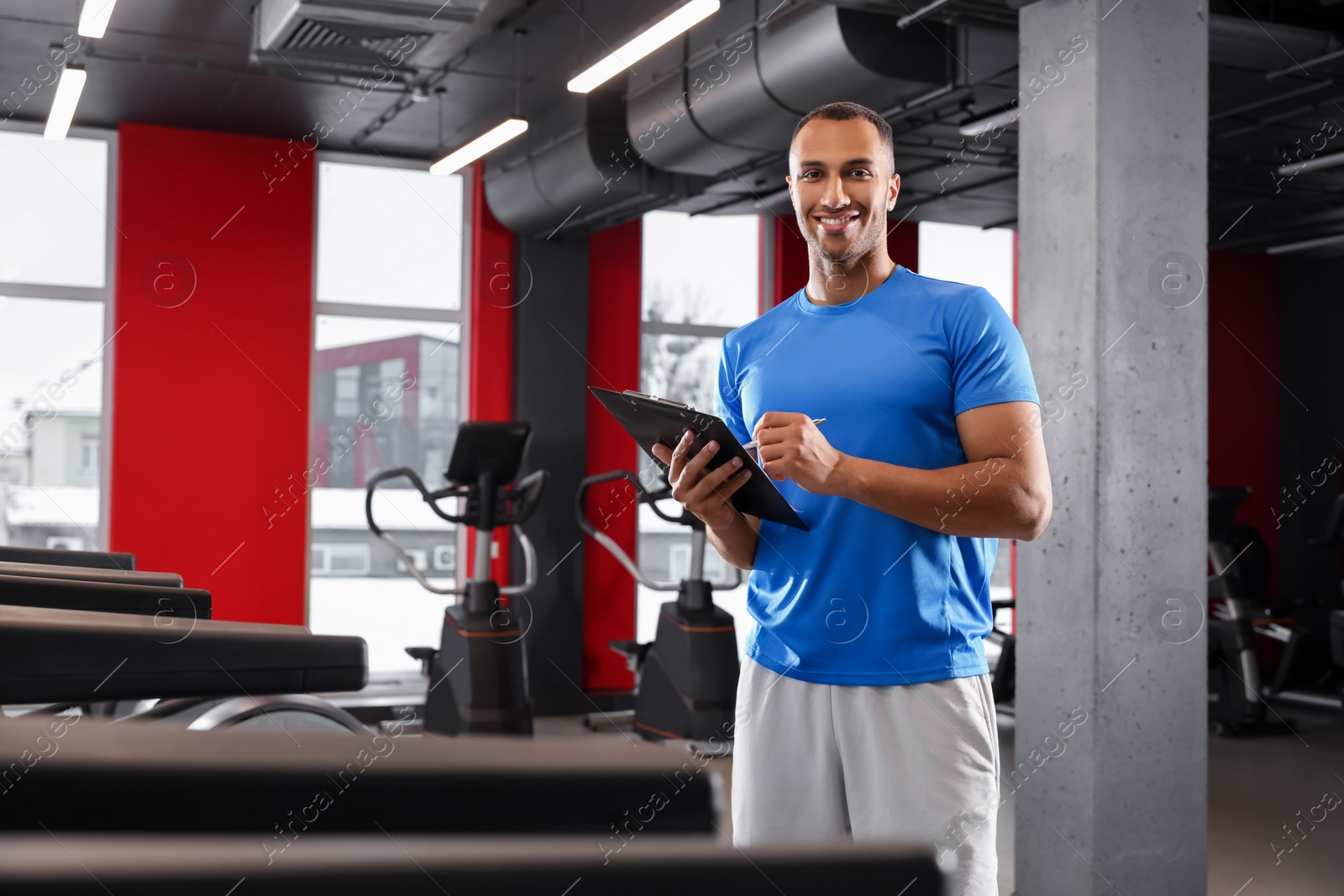 Photo of Happy trainer writing down workout plan in modern gym, space for text