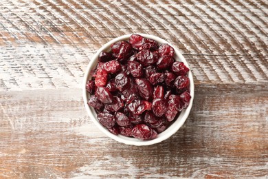 Photo of Tasty dried cranberries in bowl on rustic wooden table, top view