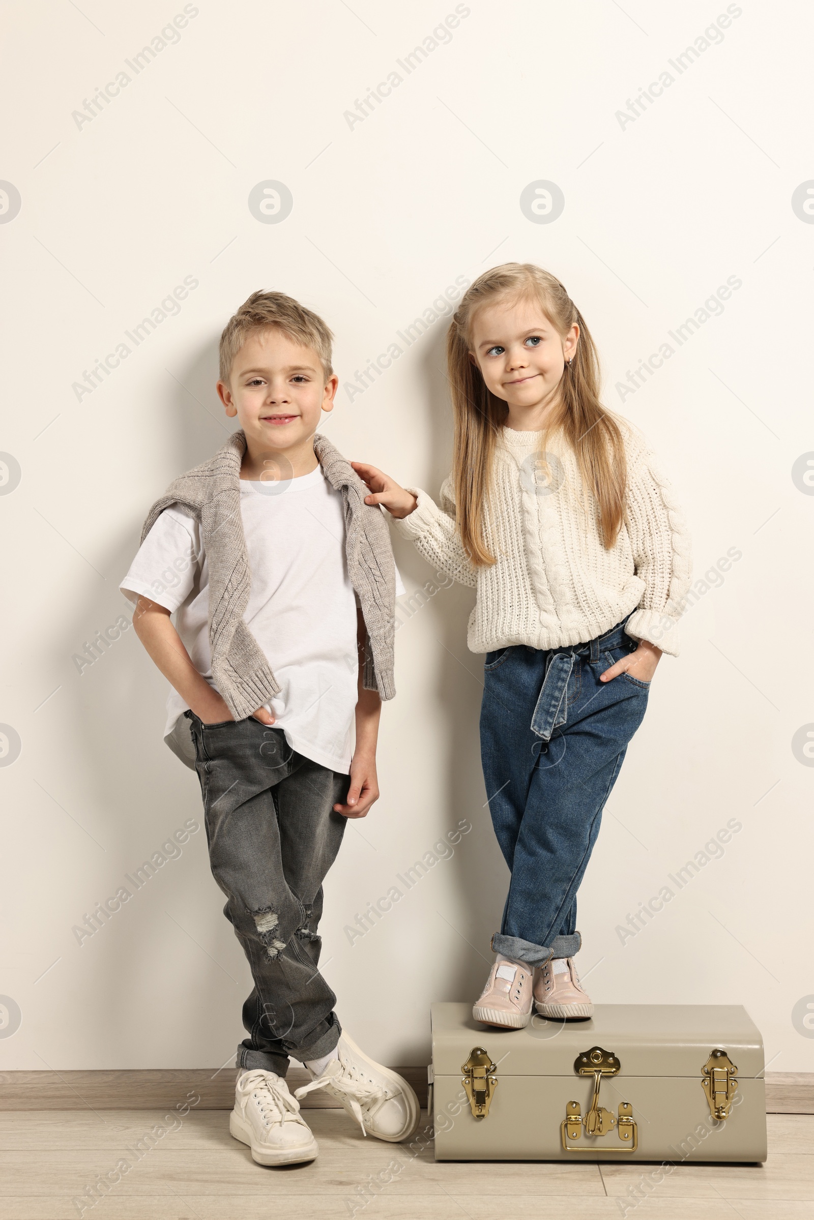 Photo of Fashion concept. Stylish children with vintage suitcase near white wall