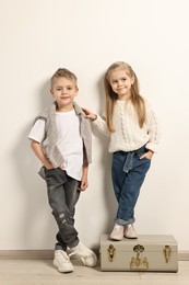 Fashion concept. Stylish children with vintage suitcase near white wall