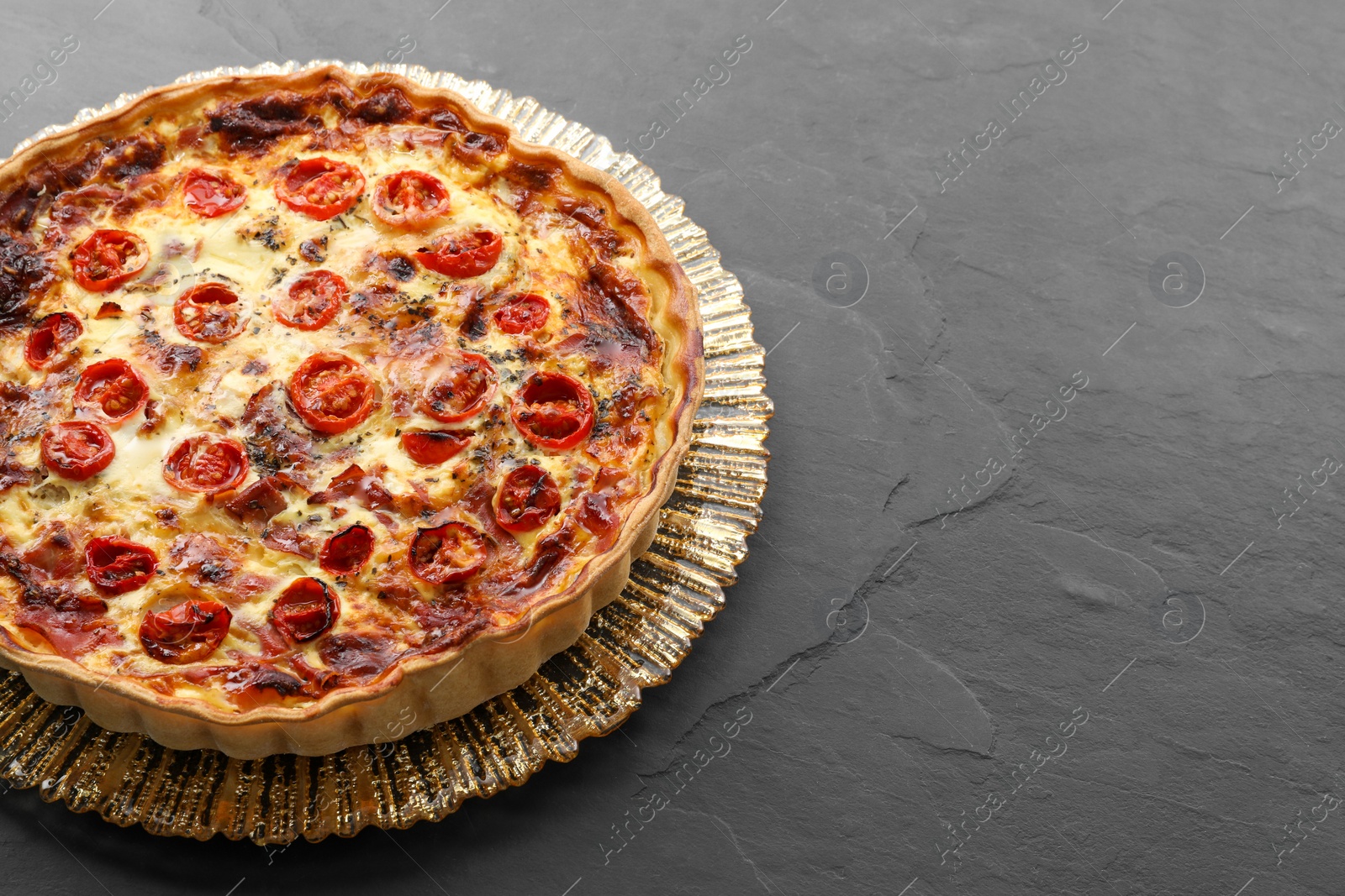 Photo of Delicious homemade quiche with prosciutto and tomatoes on black textured table