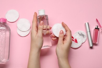 Photo of Woman with makeup remover, cotton pads, cosmetic product, lip gloss and mascara on pink background, top view