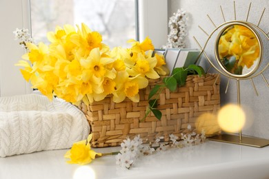 Beautiful yellow daffodils, plum tree branches, wicker basket and mirror on windowsill