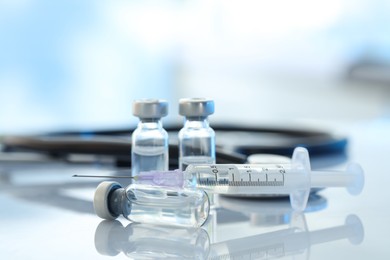 Glass vials, syringe and stethoscope on white table, closeup