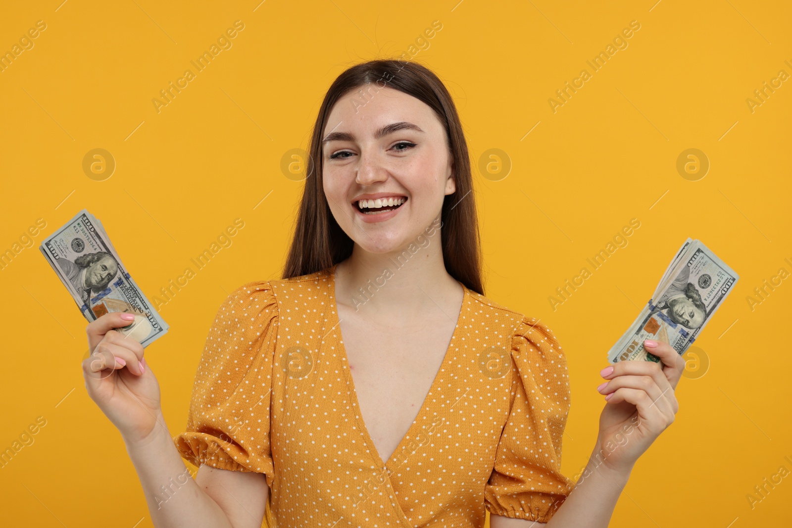 Photo of Happy woman with dollar banknotes on orange background