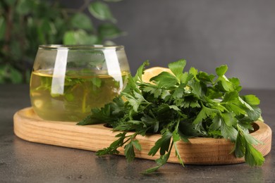 Photo of Aromatic herbal tea and fresh parsley on grey table, closeup