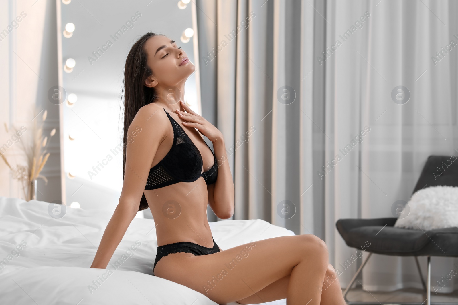 Photo of Young woman in elegant black underwear on bed indoors. Space for text