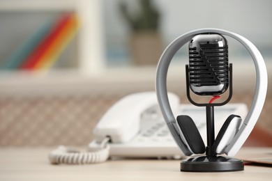 Photo of Microphone, modern headphones and desktop telephone on table indoors, space for text