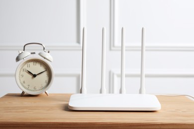 Photo of New white Wi-Fi router on wooden table near alarm clock indoors