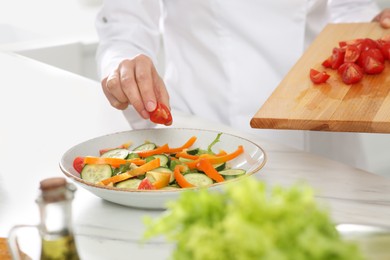 Professional chef adding cut tomato into delicious salad at white marble table, closeup