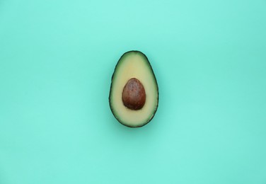 Photo of Half of tasty fresh avocado on turquoise background, top view